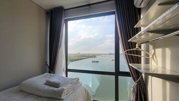 A hotel room with a large window, a bed with white linens, a bedside table, and a hanging light fixture.