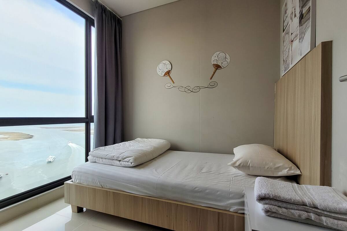 Ein modernes Schlafzimmer mit großem Fenster, einem Bett mit Kissen, einem Holzkopfteil und einer Wanddekoration.