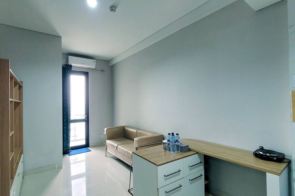 Ein Hotelzimmer mit Holzschrank, beiger Couch, kleinem Schreibtisch mit Schubladen, Wasserspender und Ablagefläche.