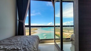 Un dormitorio con un ventanal que ofrece vista a una masa de agua y un paisaje lejano.