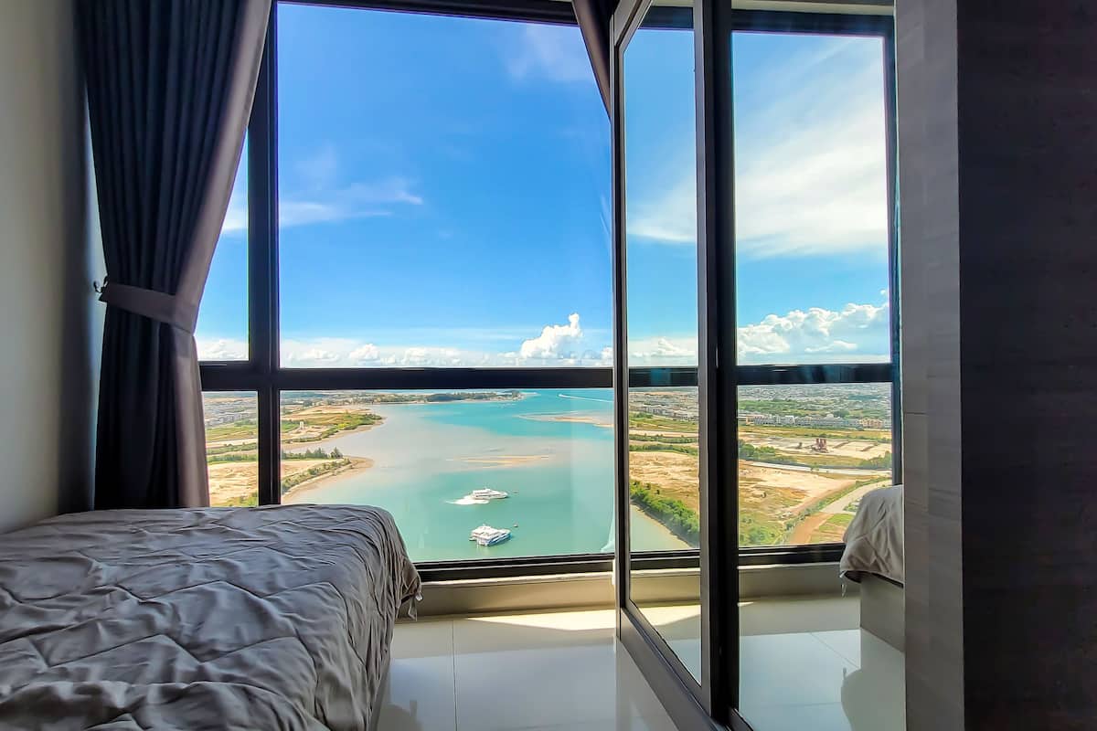 Ein Schlafzimmer mit großem Fenster und Blick auf ein Gewässer und die Ferne.