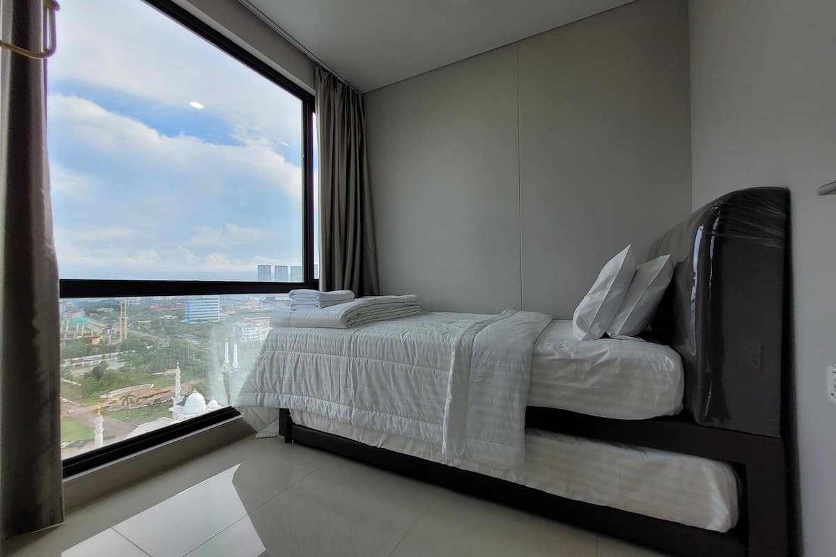 Ein modernes Schlafzimmer mit großem Fenster, einem Bett mit weißer Bettwäsche und Blick auf eine Stadtlandschaft.