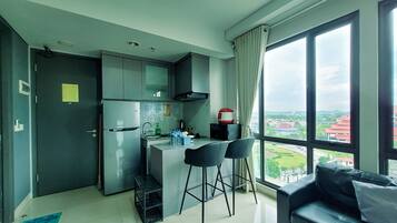 A compact kitchen with a refrigerator, a coffee maker, and a view of a cityscape through large windows.