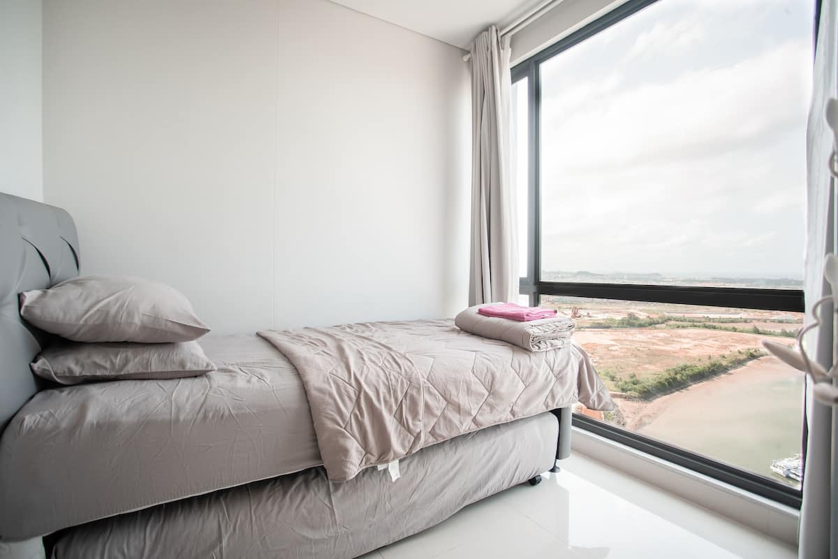 Ein modernes Schlafzimmer mit einem großen Fenster, einem Bett mit beige farbenem Duvet und Blick auf eine Landschaft.