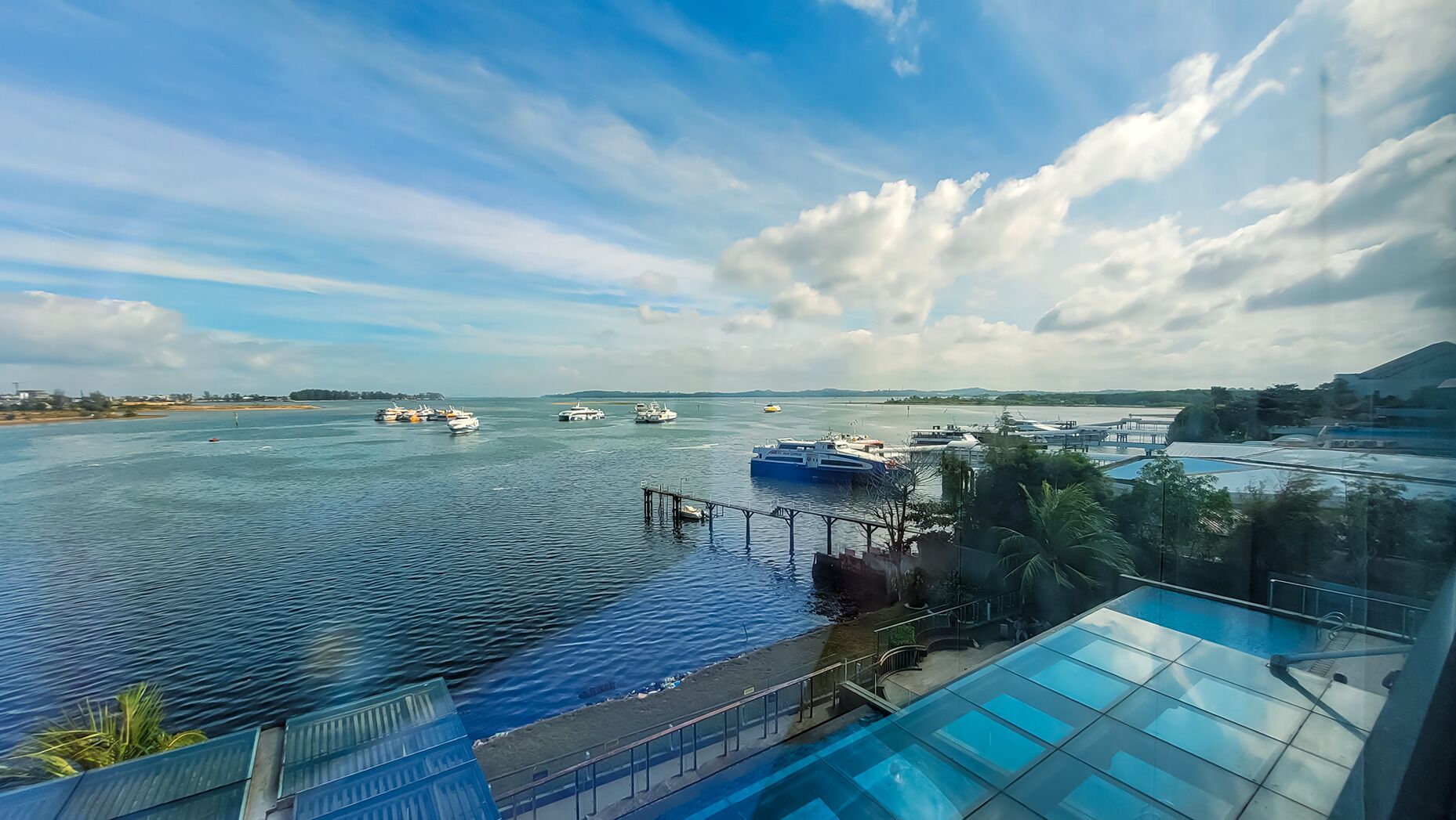 Vista de un puerto deportivo con varias embarcaciones amarradas, una piscina con fondo de cristal y cielo despejado.