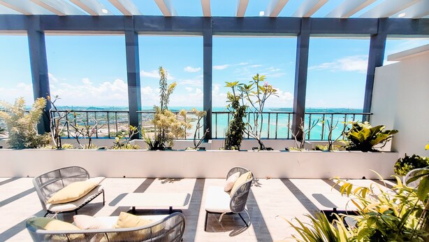 Balcón con mobiliario exterior y plantas en macetas, con vista a la playa y al océano.