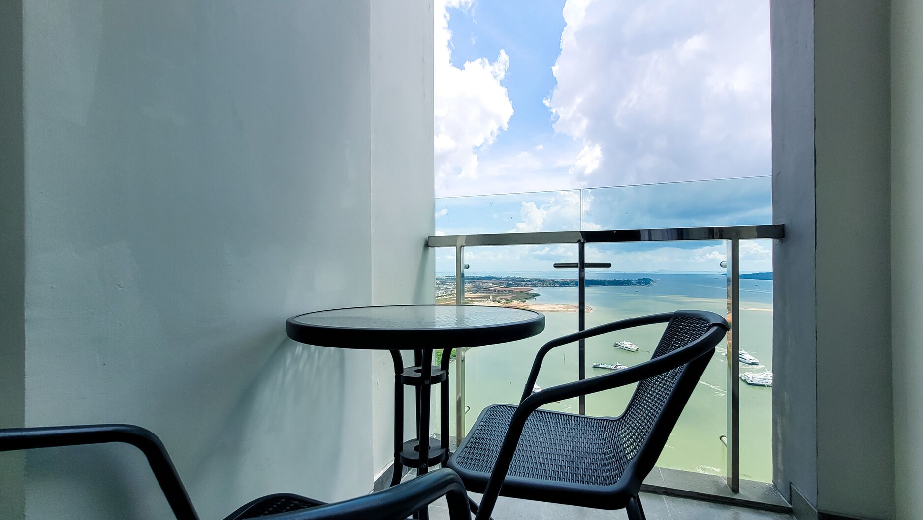 A balcony with a table and chairs, overlooking a body of water with boats and a distant shoreline.