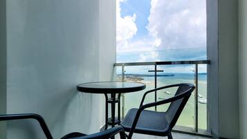 A balcony with a table and chairs, overlooking a body of water with boats and a distant shoreline.