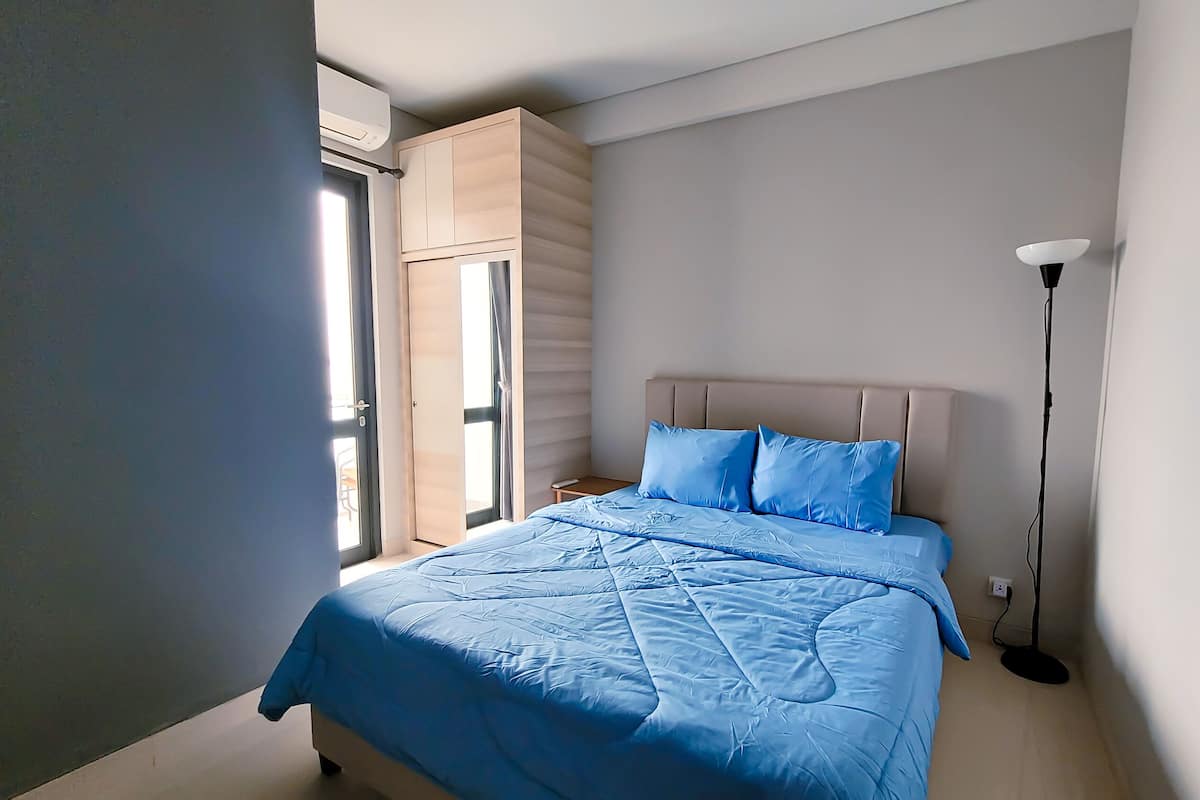 Quarto com cama, mesa de cabeceira, abajur e guarda-roupa.