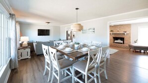 A modern dining area with a wooden table set for six, white chairs, and a hanging light fixture. - Palmetto Point - Game Room + Pool (Wilmington)