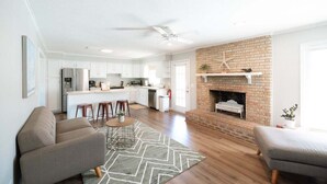 A modern living room with a fireplace, a kitchen in the background, and a dining area with stools. - Palmetto Point - Game Room + Pool (Wilmington)
