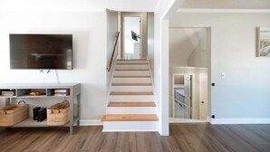 A staircase leading to a second floor, a flat-screen TV mounted on the wall, and a console table with baskets and books. - Palmetto Point - Game Room + Pool (Wilmington)