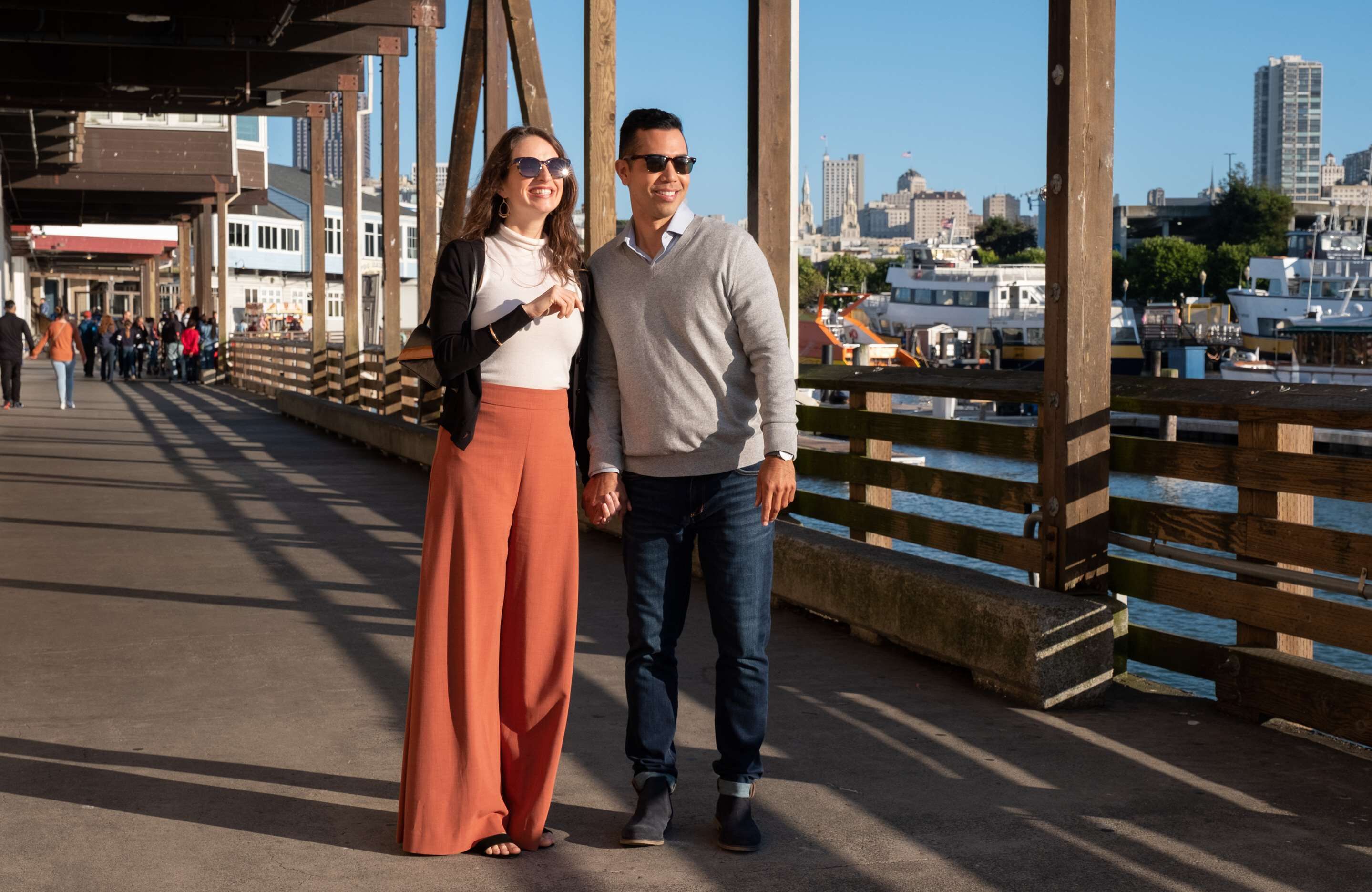 A couple standing on a bridge with a city skyline in the background.