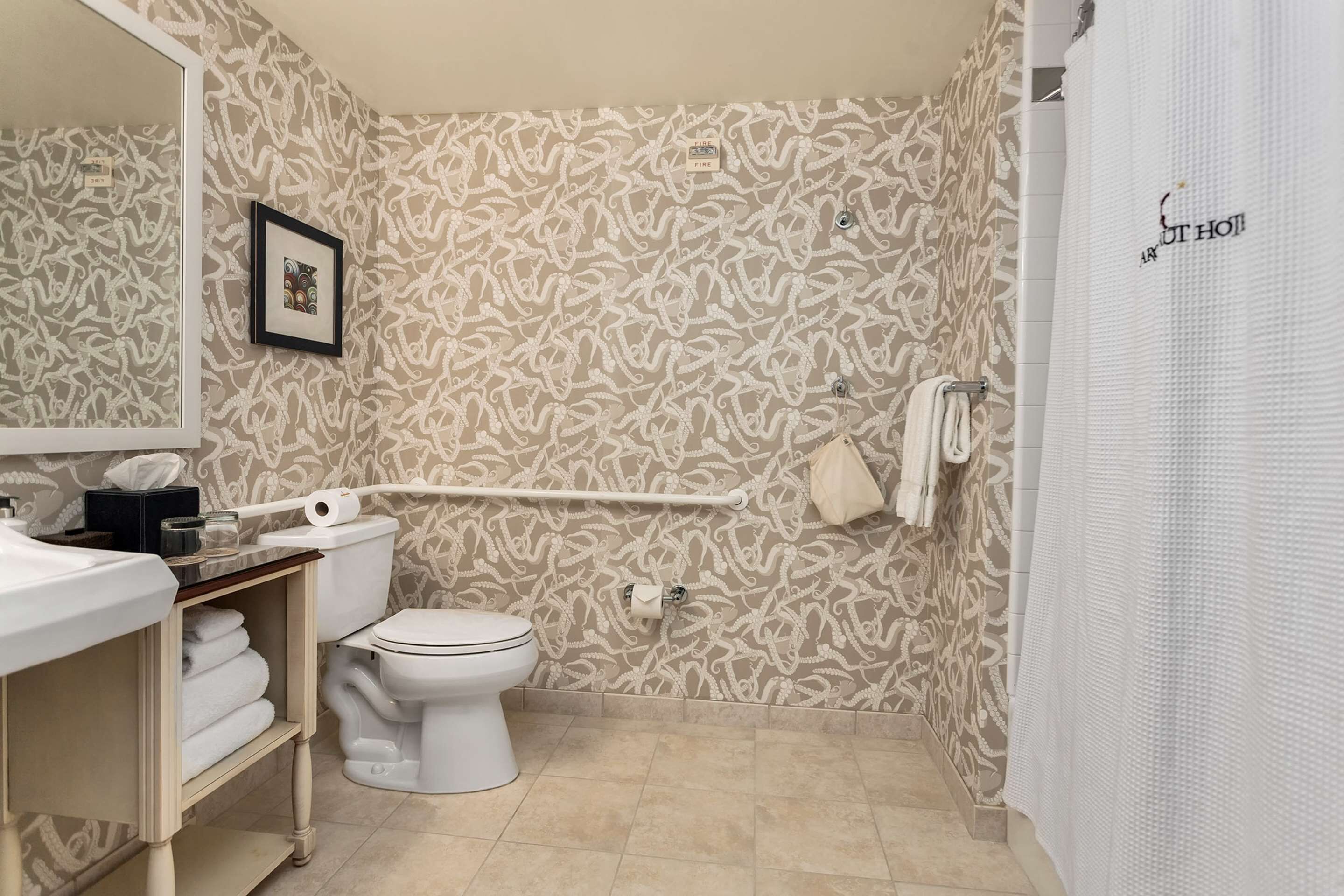 A bathroom with a patterned wallpaper, a toilet, a sink with a mirror, and a shower curtain.