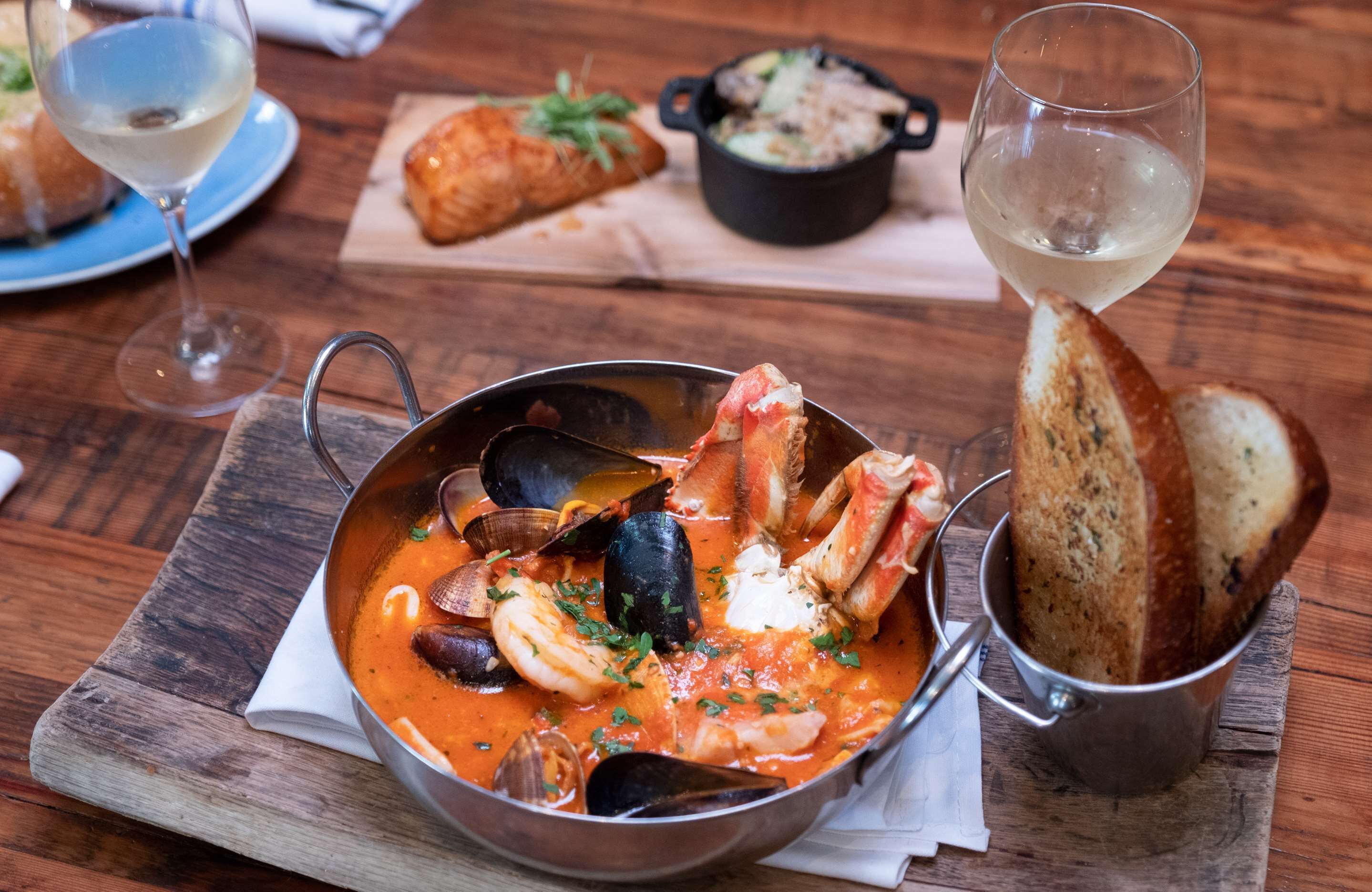 Un plat de fruits de mer servi avec du pain et du vin sur une table en bois.