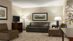 Une chambre d’hôtel équipée d’un canapé, d’un fauteuil, d’un téléviseur à écran plat, d’un bureau et d’une lampe.