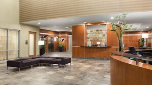 A reception area with a curved reception desk, a seating area with a sofa, an elevator, and a wall with a bulletin board.