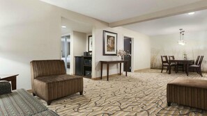 Une chambre d’hôtel avec un tapis à motifs, un canapé, une table à manger avec des chaises et une petite table sur laquelle est posé un vase.