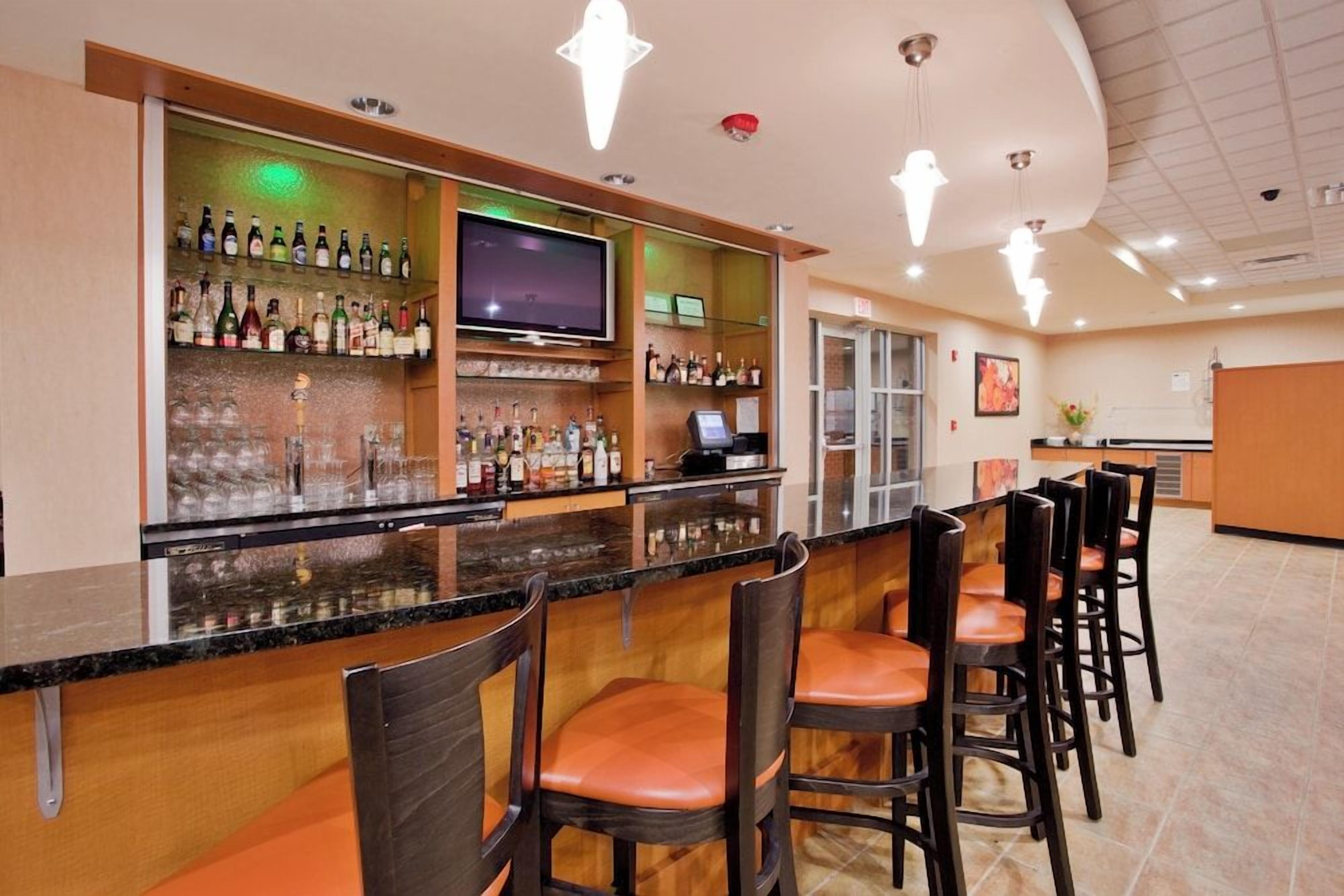 A bar area with a flat-screen TV, multiple liquor bottles, and bar stools.