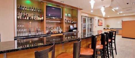 A bar area with a flat-screen TV, multiple liquor bottles, and bar stools.