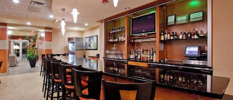 A bar area with a long counter, multiple bar stools, and a television screen.