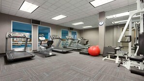 A gym with treadmills, elliptical machines, a red exercise ball, and weightlifting equipment.