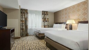 Habitación de hotel con dos camas, televisión, escritorio con cajones y alfombra estampada.