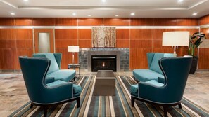 A hotel lobby with a fireplace, two armchairs, a coffee table, and a striped rug.