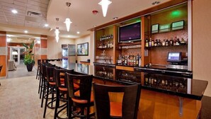 Una zona de bar con una barra larga, varios taburetes, un televisor y estantes llenos de botellas.