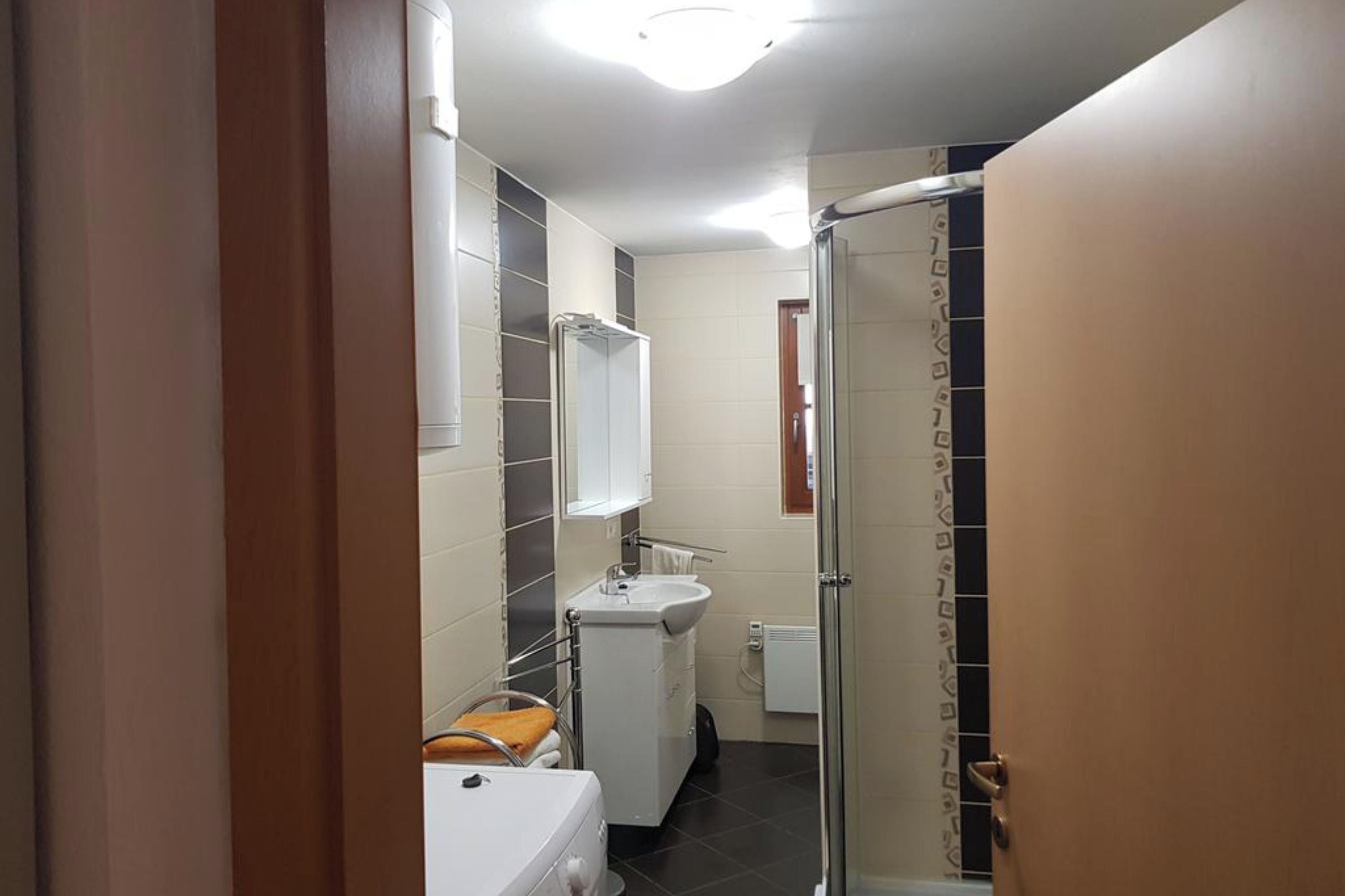 A narrow bathroom with a white sink, a mirror, and a shower area.