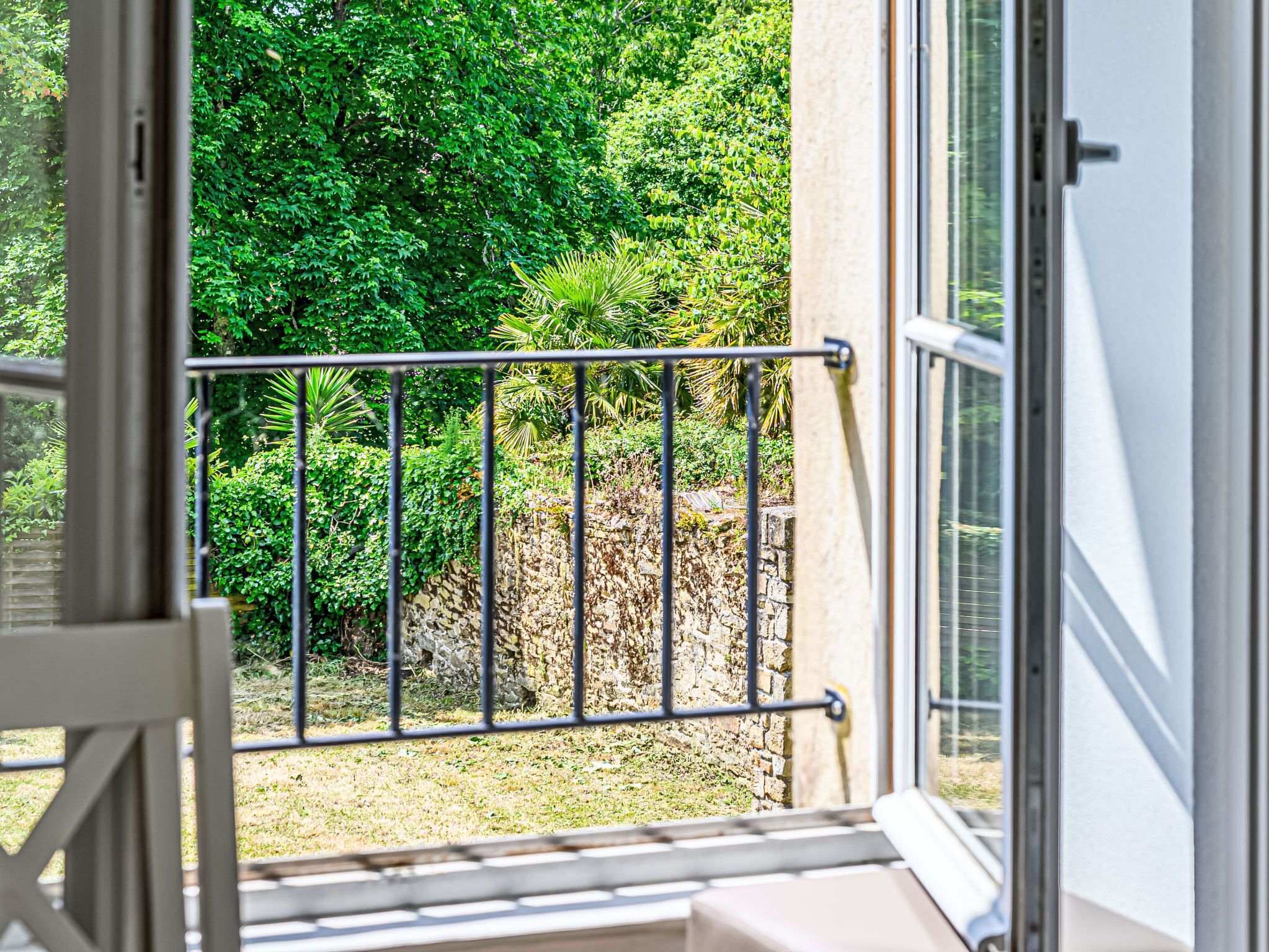 A balcony with a metal railing overlooking a garden with various plants and a stone wall.