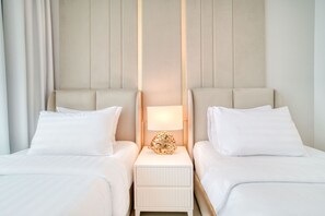 Hotellihuone, jossa on kaksi sänkyä, yöpöytä lampun kanssa ja neutraalin sävyinen sängynpääty.