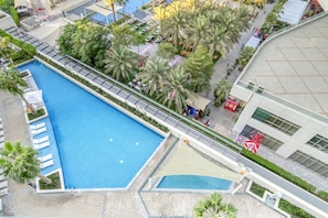 Vue aérienne d’un hôtel doté d’une grande piscine rectangulaire, entourée de palmiers et de chaises longues.