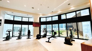 Une salle de sport moderne équipée de divers appareils d’exercice, dotée de grandes fenêtres et offrant une vue sur les bâtiments environnants.