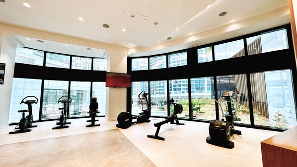 A modern gym with various exercise equipment, large windows, and a view of buildings outside.