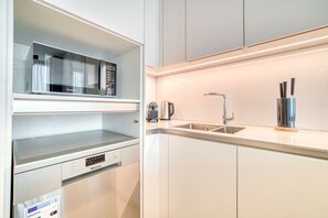 Une cuisine moderne équipée d’un four à micro-ondes encastré, d’une machine à café et d’un évier en acier inoxydable.