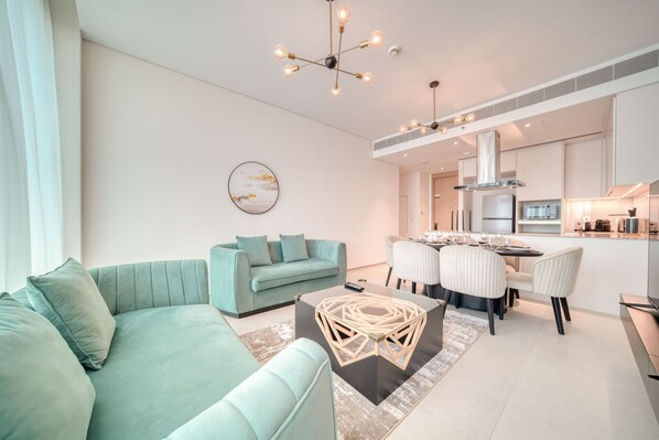 A modern living room with a teal sofa, a glass coffee table, and a dining area with a white table and chairs.