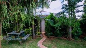 Un jardín con una mesa de picnic de madera, un sendero de piedra y diversas plantas tropicales.