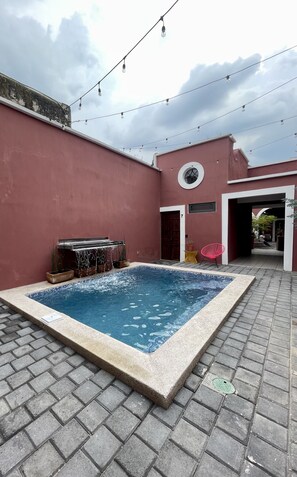 A rectangular swimming pool with a tiled edge, surrounded by a paved patio. There is a small waterfall feature on one side, and a door leading to an adjacent building. - Quinta la Perla (Guadalajara)
