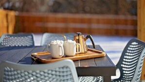 A wooden table with a tray holding two white mugs and a gold coffee pot, set on an outdoor patio with metal chairs. - Newly Built Bloomington Oasis: 4bd/2.5br & Backyard, 10mins to IUB & Downtown (Bloomington)