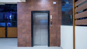 An elevator in a modern building with a metallic finish and a red-tiled wall. - MUGUNDAN 'S  SMART STAY (Coimbatore)