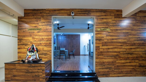 A reception area with a wooden wall, a reception desk, and a view into the interior. - MUGUNDAN 'S  SMART STAY (Coimbatore)