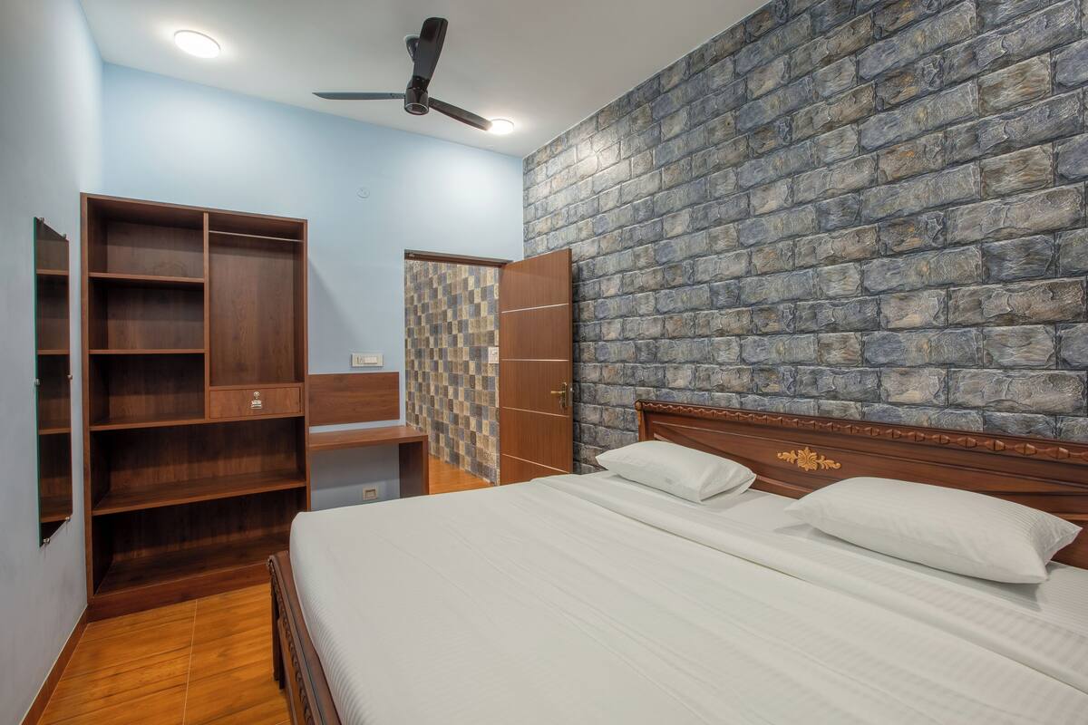A bedroom with a large bed, wooden wardrobe, and a ceiling fan.