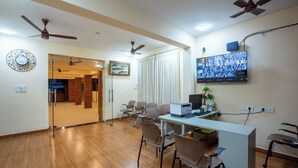 A spacious room with wooden flooring, ceiling fans, a desk with a computer, multiple chairs, and a television mounted on the wall. - MUGUNDAN 'S  SMART STAY (Coimbatore)