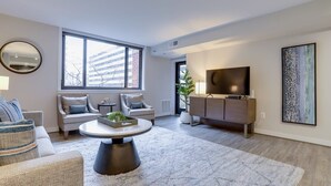 A modern living room with a sofa set, a coffee table, a TV, and a large window. - Sojourn | Courtland Towers (Arlington)