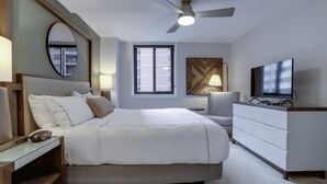 A modern bedroom with a bed, bedside table, TV, and a ceiling fan. - Sojourn | Courtland Towers (Arlington)