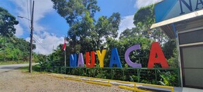 A sign with the name 'Nauyaca' in colorful letters, a gravel path, and a building with a blue roof in the background.