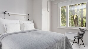 A bedroom with a large bed, a window with a view of trees, and a chair by the window. - Saunamäki Resort Guesthouse - Countryside Views (Salo)