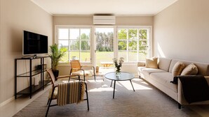 A living room with a sofa, chairs, a TV, and a large window offering a view of a grassy area. - Saunamäki Resort Guesthouse - Countryside Views (Salo)