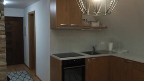 Cozinha compacta com armários de madeira, forno embutido e uma luminária pendente moderna.
